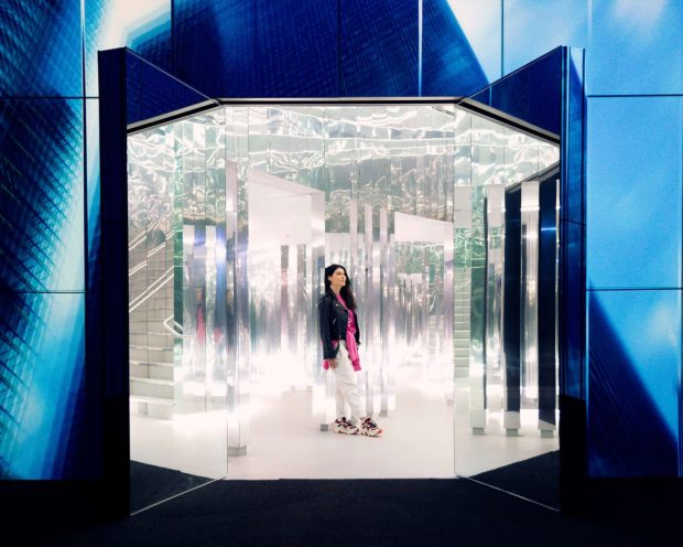 WOMAN STANDS AMIDST MIRRORS IN MIAMI’S IMMERSIVE ART MUSEUM CALLED SUPERBLUE IN INSTALLATION CALLED THE FOREST OF US