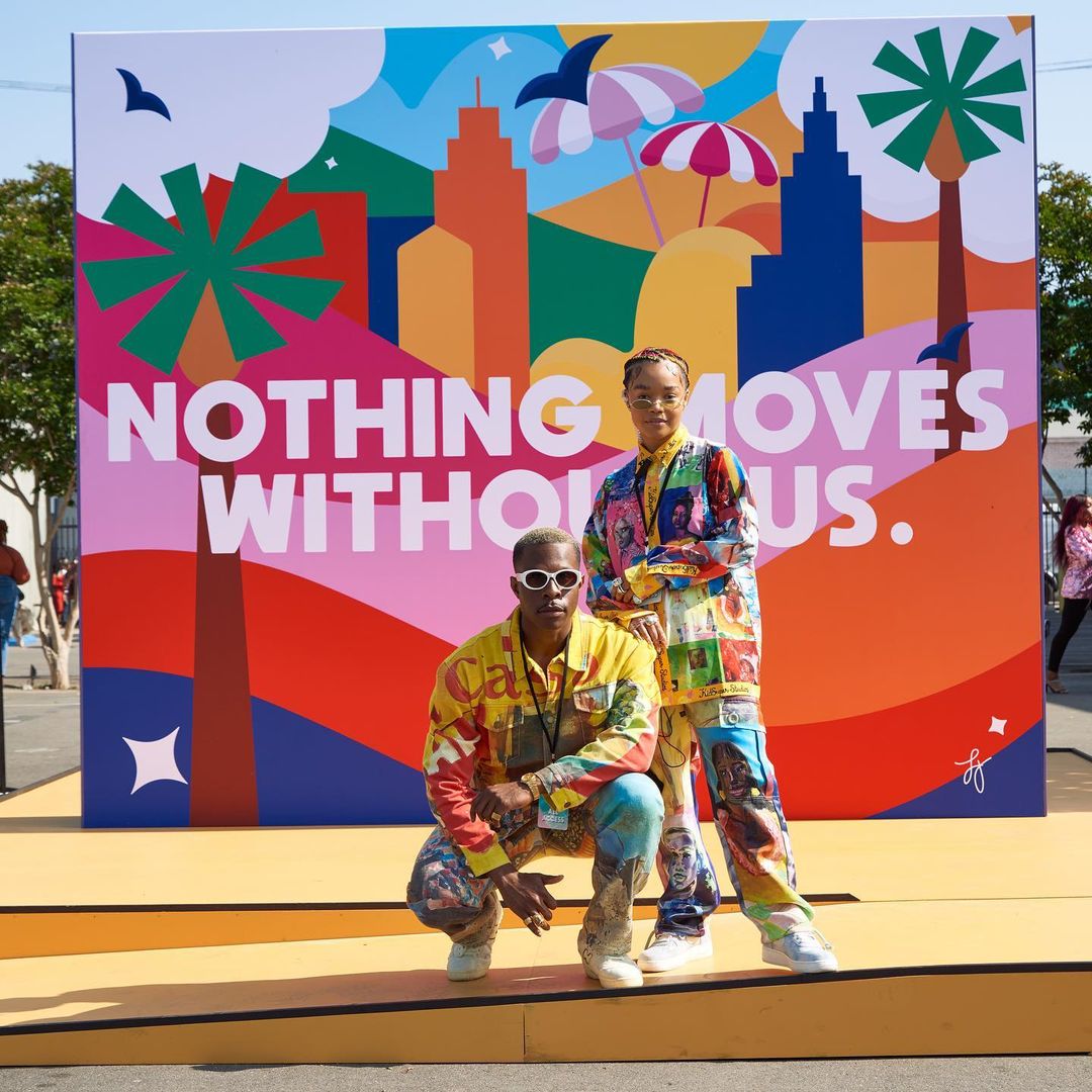 TWO PEOPLE POSE IN FRONT OF “NOTHING MOVES WITHOUT US.” WRITTEN ON COLORFUL BACKDROP AT CULTURECON NYC EVENT