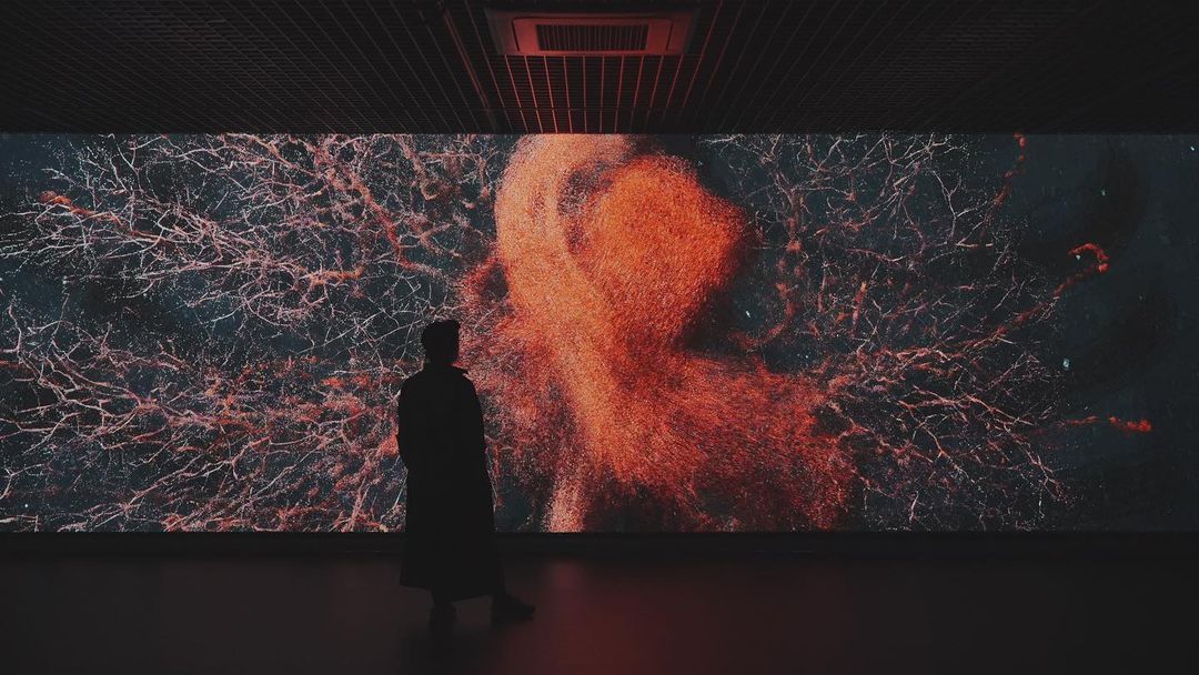 MAN ADMIRES MARSHMALLOW LASER FEAST’S RED AND ORANGE IMMERSIVE SCREEN INSTALLATION CALLED EVOLVER