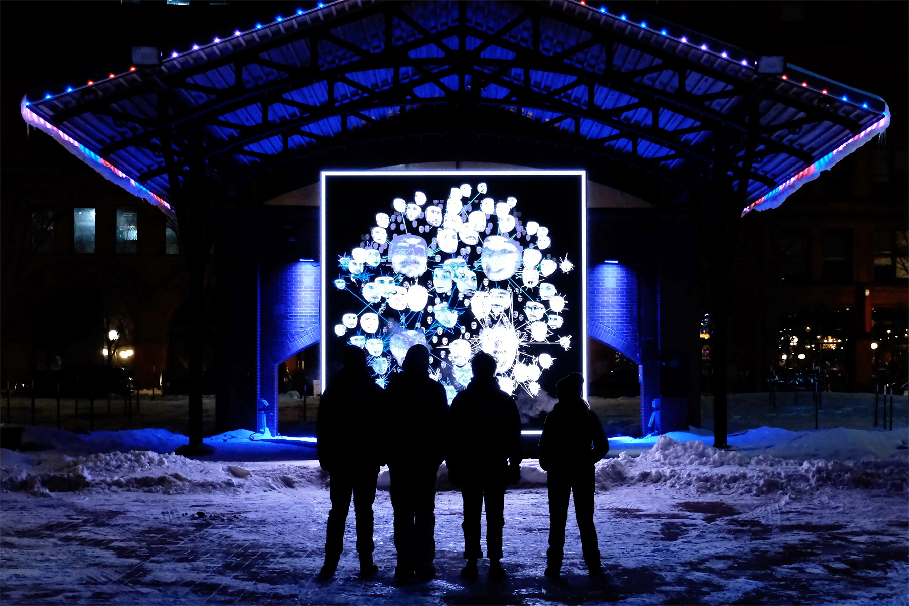 PEOPLE IN SNOW STARING UP AT INTERACTIVE DIGITAL SCREEN INSTALLATION OF FACES IN IREGULAR’S OUR COMMON HOME