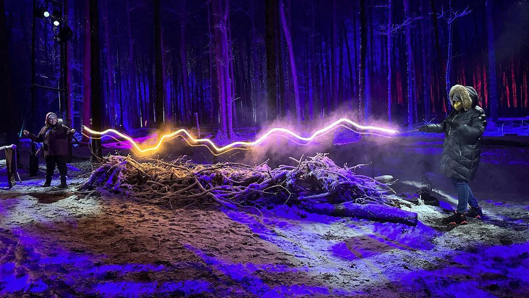 TWO PEOPLE HOLD WANDS IN FOREST WITH NEON LIGHT CONNECTING THEM IN HARRY POTTER: A FORBIDDEN FOREST EXPERIENCE