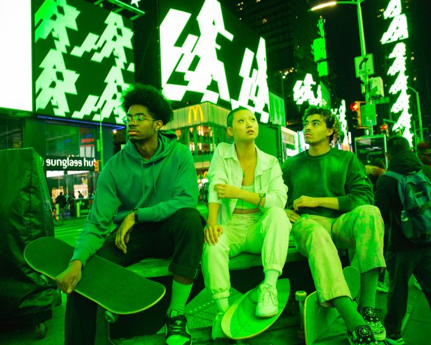 THREE INDIVIDUALS SIT ON BENCH LOOKING UP AT ALGORAND’S NEON GREEN CARBON-NEGATIVE BLOCKCHAIN INSTALLATION CALLED LIGHTS OUT AT TIMES SQUARE