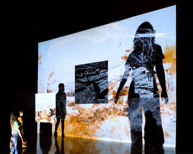 PEOPLE STARE UP AT THEIR DISTORTED REFLECTIONS ON LARGE SCREEN IN MENTAL MAPS BY IREGULAR
