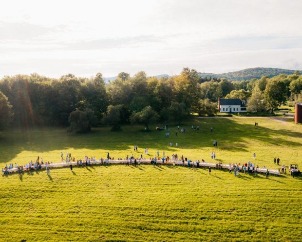 LONG OUTDOOR TABLE WITH GUESTS CONVENING IN OUTSTANDING IN THE FIELD