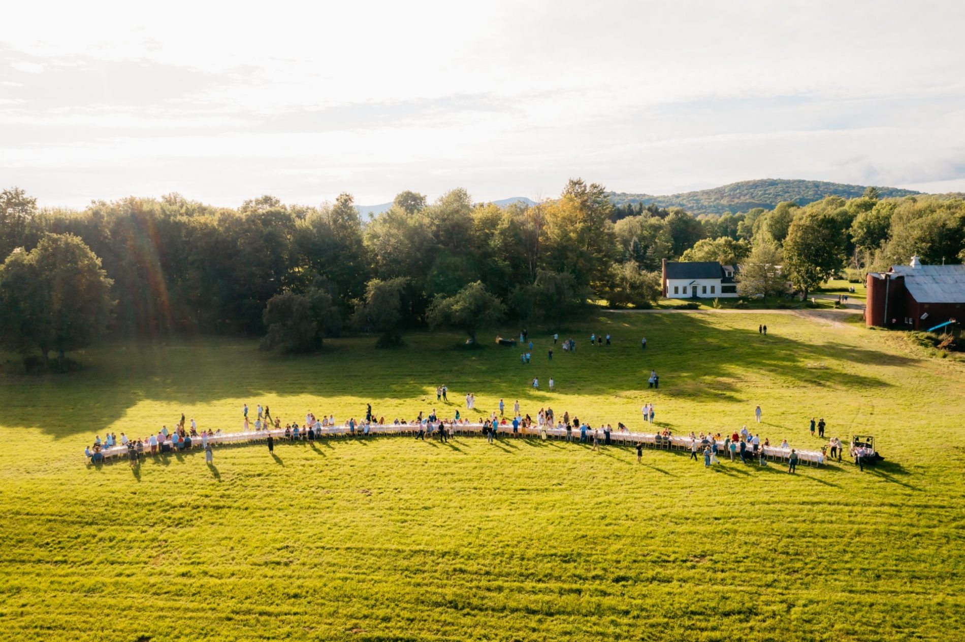 LONG OUTDOOR TABLE WITH GUESTS CONVENING IN OUTSTANDING IN THE FIELD