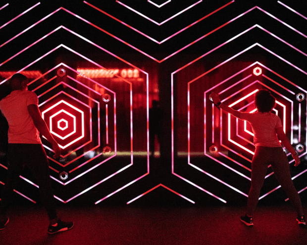 TWO INDIVIDUALS STAND NEXT TO EACH OTHER AS THEY PLACE THEIR HANDS ON A RED LINED WALL AT UNDER ARMOUR RUSH LAB