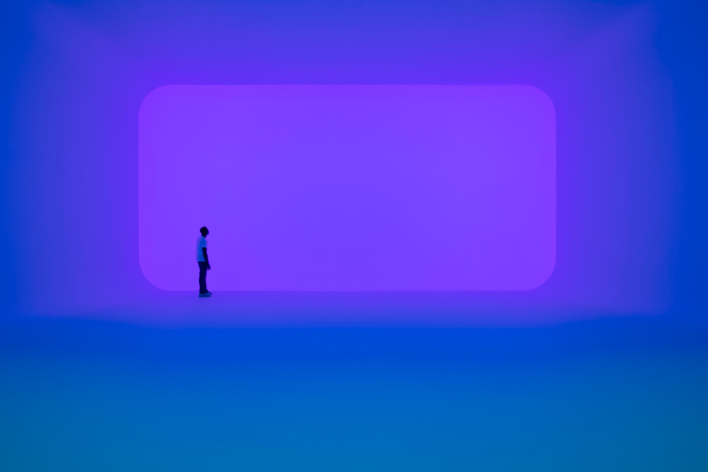 MAN STANDS IN BLUE ROOM WITH PURPLE WALL IN SUPERBLUE MIAMI’S IMMERSIVE INSTALLATION SPACE