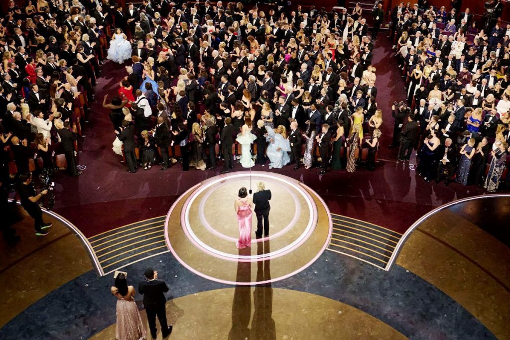 March XP: A grand award show with a packed audience, as two presenters stand on an illuminated stage addressing the crowd
