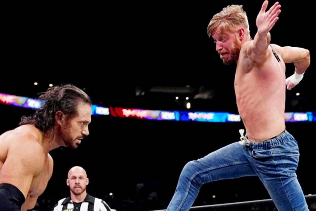 March XP: High-energy wrestling match, as a competitor in jeans leaps into action against his opponent in a packed arena.